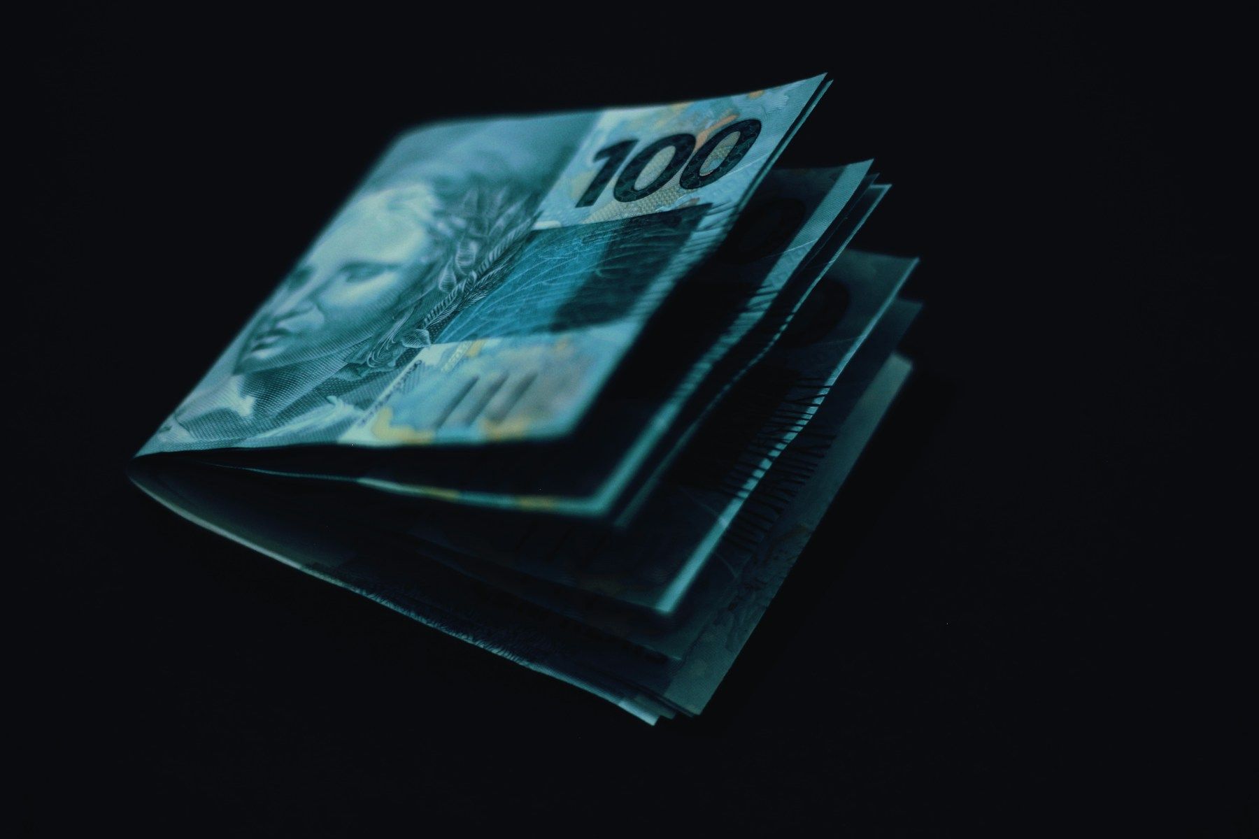 Cédulas de cem reais dobradas sobre fundo escuro