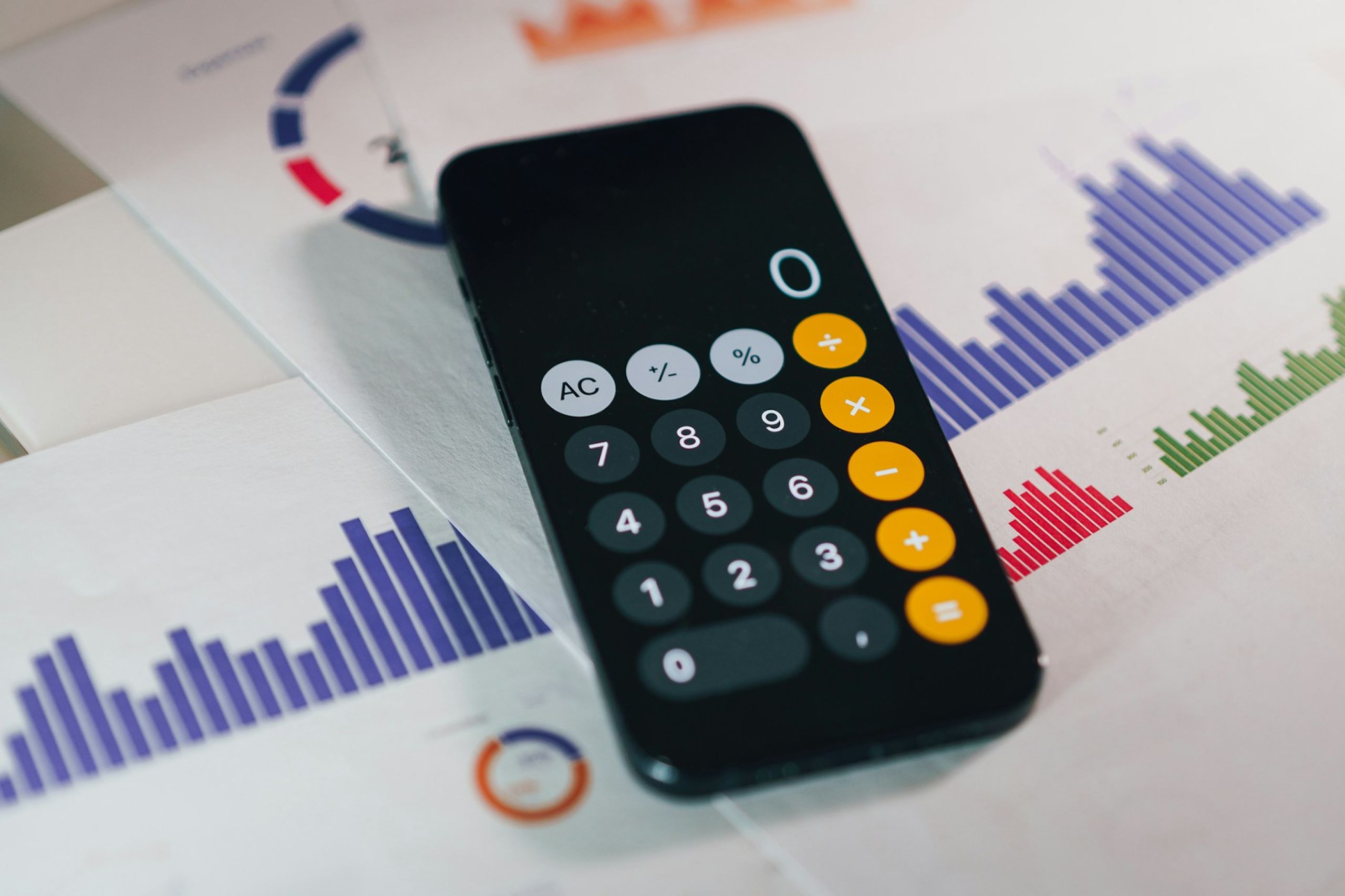 Calculadora aberta em celular sobre relatórios impressos com gráficos de barras e pizza